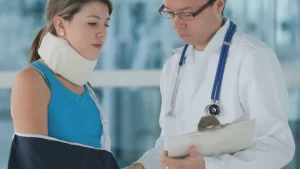Injured woman with neck brace and arm sling consulting with a doctor.