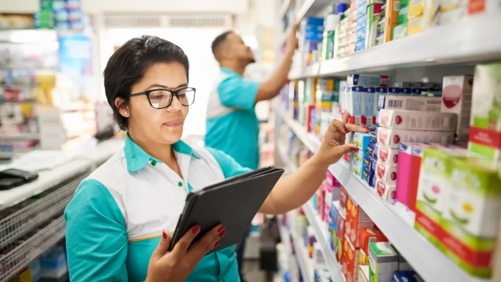 Pharmacy employees organizing shelves while using a tablet for inventory.